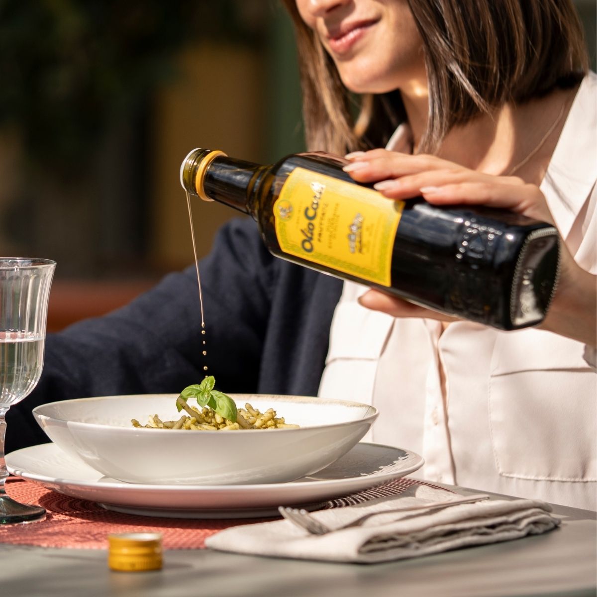 Donna che versa un filo di OLIO CARLI Extra Vergine di Oliva Fruttato su un paitto di pasta