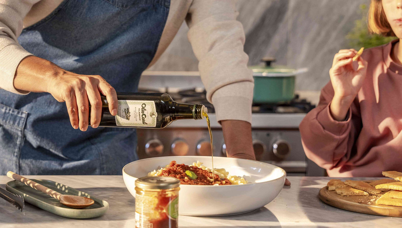 Papà e figlia a tavola completano una pasta al sugo con un filo di OLIO CARLI Extra Vergine di Oliva Classico