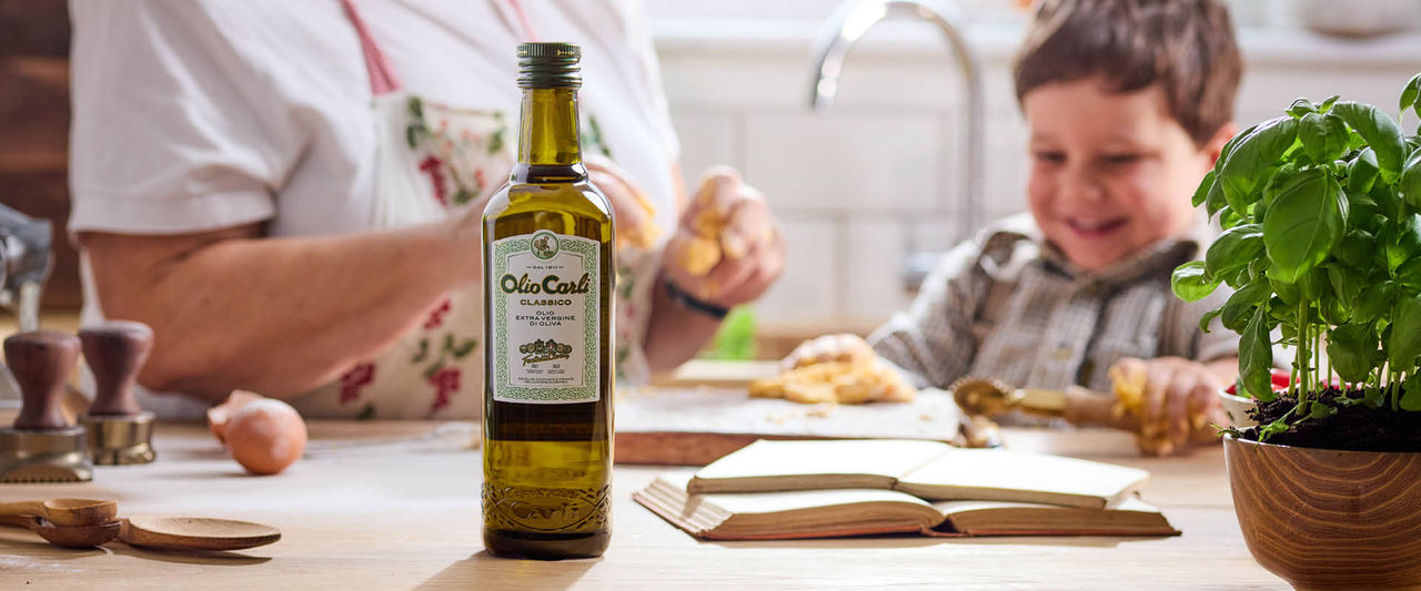 Bottiglia di Olio di Oliva Carli Extra Vergine classico in ambientazione domestica con nonna e nipote che cucinano