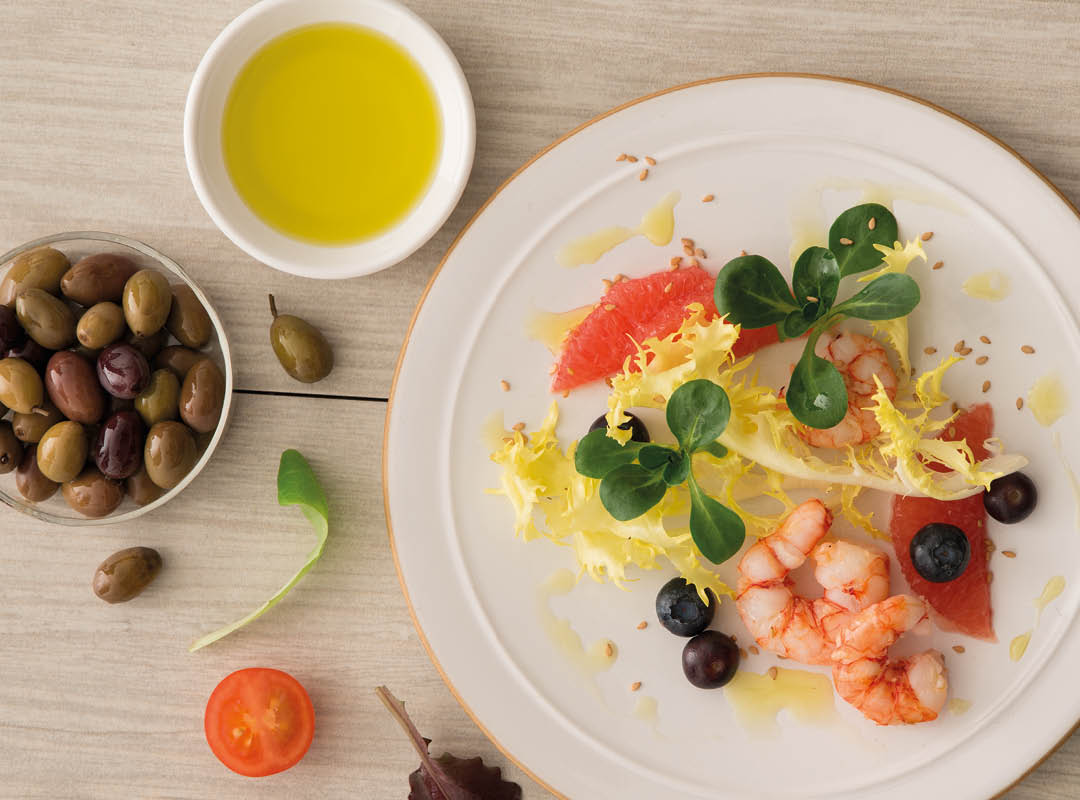 Piatto di insalata e gamberi con ciotola di olio e olive